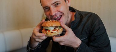 Mutlu adam fast food yiyor, hamburger. Bir adam masada oturuyor ve çizburger yiyor.