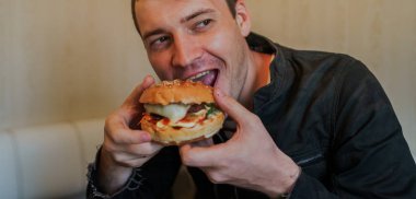 Mutlu adam fast food yiyor, hamburger. Bir adam masada oturuyor ve çizburger yiyor.