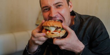 Mutlu adam fast food yiyor, hamburger. Bir adam masada oturuyor ve çizburger yiyor.