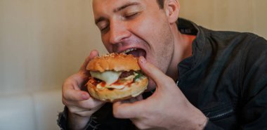 Genç adam hamburger yiyor. Bir adam masada oturuyor ve fast food kafede çizburger yiyor..