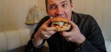 Genç adam hamburger yiyor. Bir adam masada oturuyor ve fast food kafede çizburger yiyor..