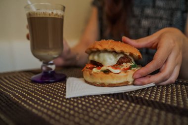 Kadınların elleri taze lezzetli burgerleri tutuyor. Ellerinde lezzetli bir hamburger var. Fast food yemeği..