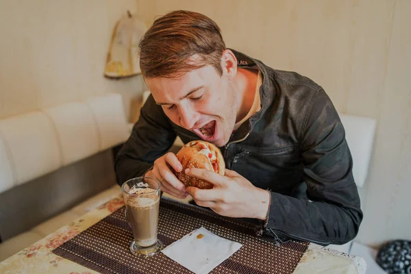 快乐的人在吃快餐汉堡包一个男人坐在桌旁吃着芝士汉堡 — 图库照片
