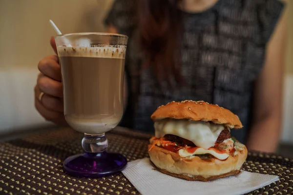 Food-Fotografie. Heißer Cappuccino mit Hamburger am Tisch im Fast-Food-Café. Cheeseburger und Kaffee auf dem Tisch, Getränk enthält Koffein. — Stockfoto