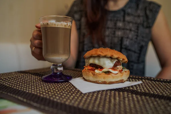 Fotka jídla. Hot cappuccino s hamburgerem u stolu v kavárně rychlého občerstvení. Cheeseburger a káva na stole, nápoj obsahuje kofein. — Stock fotografie