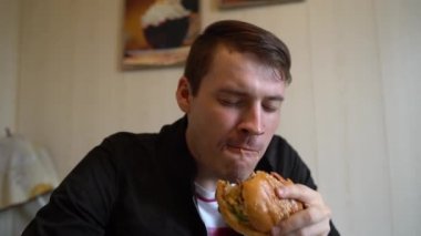 Genç adam hamburger yiyor. Bir adam masada oturuyor ve fast food kafede çizburger yiyor..