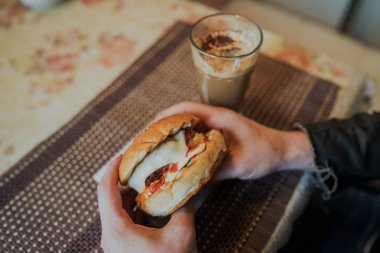 Yemek fotoğrafçılığı. Fast food kafedeki masada hamburgerli sıcak kapuçino. Masanın üzerinde çizburger ve kahve, içkinin içinde kafein var..