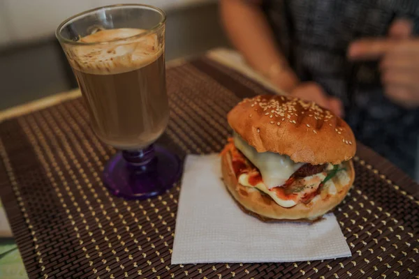 Food-Fotografie. Heißer Cappuccino mit Hamburger am Tisch im Fast-Food-Café. Cheeseburger und Kaffee auf dem Tisch, Getränk enthält Koffein. — Stockfoto