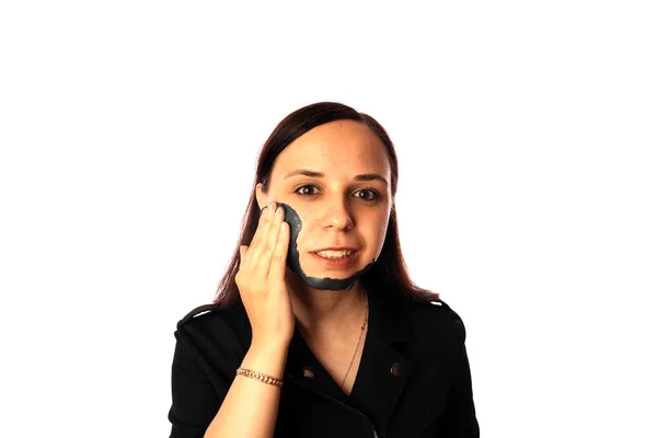 Une jeune femme inflige un masque noir sur le visage isolé sur fond blanc.Le concept de mode de vie sain, de beauté, de soins du corps . — Photo