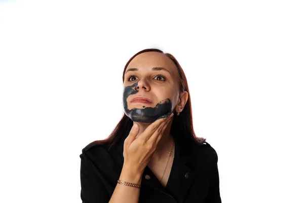 Een jonge vrouw legt een zwart masker op het gezicht geïsoleerd op witte achtergrond.Het concept van gezonde levensstijl, schoonheid, lichaamsverzorging. — Stockfoto