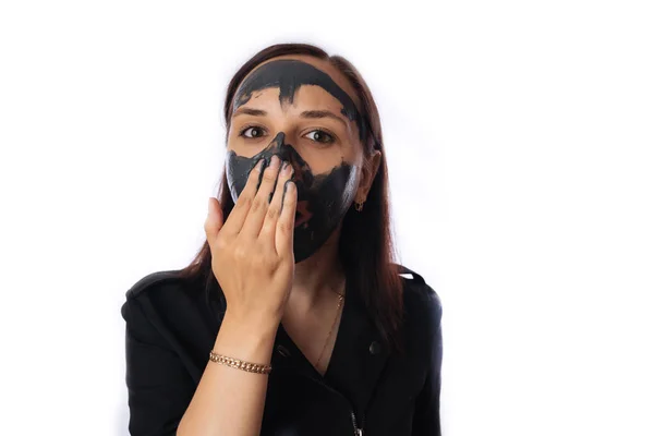 Una mujer joven inflige una máscara negra en la cara aislada sobre fondo blanco.El concepto de estilo de vida saludable, belleza, cuidado corporal . — Foto de Stock