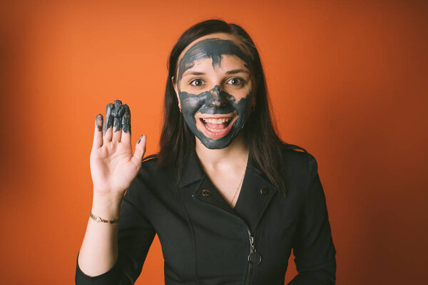 A young woman inflicts a black mask on the face on an orange background. The concept of healthy lifestyle, beauty, body care.