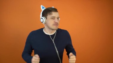 Kulaklıklı genç adam turuncu arka planda dans ediyor..
