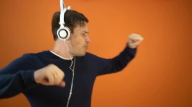 Kulaklıklı genç adam turuncu arka planda dans ediyor..