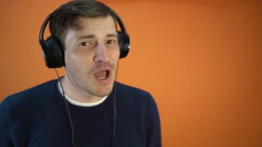 Kulaklıklı genç adam turuncu bir arka planda şarkı söylüyor..