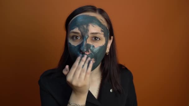 Uma Jovem Mulher Inflige Uma Máscara Preta Rosto Fundo Laranja — Vídeo de Stock