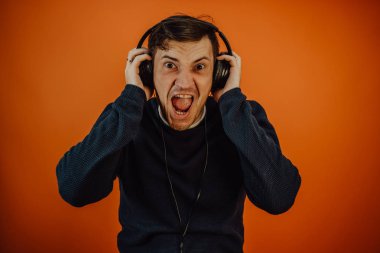 Kulaklıklı, güzel bir genç adam turuncu bir arka planda dans ediyor. Uluslararası Müzik Günü konsepti.