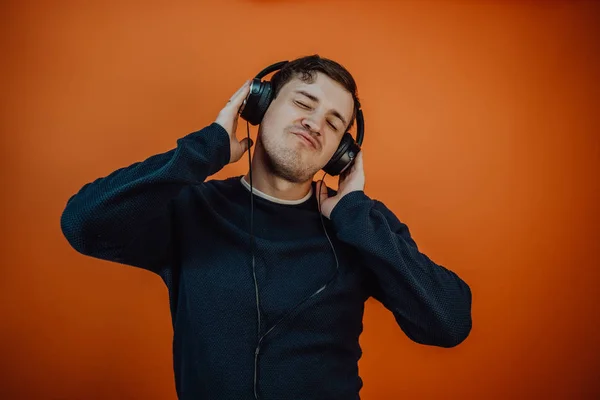 A beautiful young man in headphones with ears is dancing on an orange background. The concept of International Music Day. — Stock Photo, Image