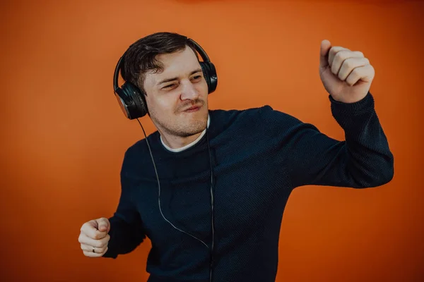 Un beau jeune homme aux écouteurs avec des oreilles danse sur fond orange. Le concept de la Journée internationale de la musique. — Photo