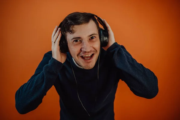 Ein schöner junger Mann mit Kopfhörern und Ohren tanzt auf orangefarbenem Hintergrund. Das Konzept des Internationalen Tages der Musik. — Stockfoto