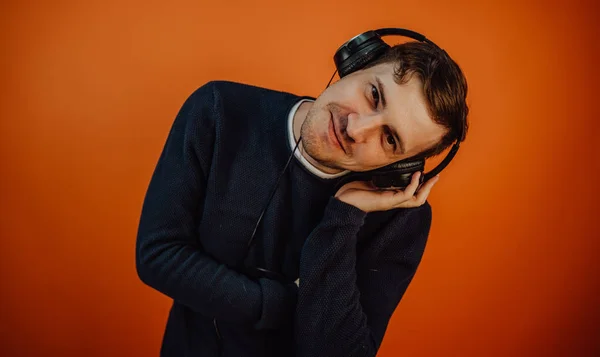 Un beau jeune homme aux écouteurs avec des oreilles danse sur fond orange. Le concept de la Journée internationale de la musique. — Photo