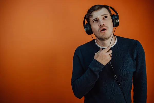 Ein schöner junger Mann mit Kopfhörern und Ohren tanzt auf orangefarbenem Hintergrund. Das Konzept des Internationalen Tages der Musik. — Stockfoto