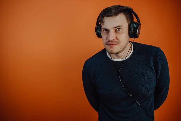 Un joven hermoso en audífonos con orejas está bailando en un fondo naranja. El concepto del Día Internacional de la Música. — Foto de Stock