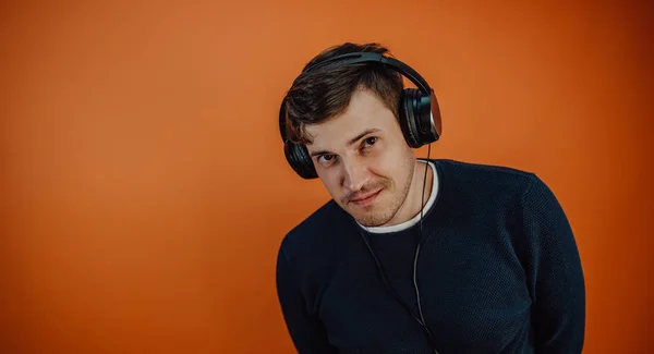 Un joven hermoso en audífonos con orejas está bailando en un fondo naranja. El concepto del Día Internacional de la Música. — Foto de Stock