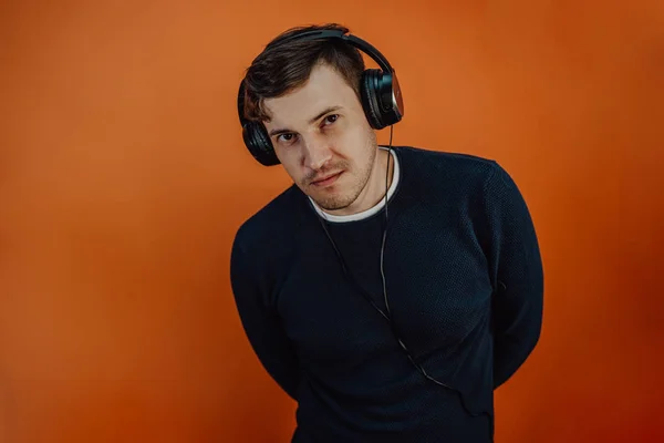 Un joven hermoso en audífonos con orejas está bailando en un fondo naranja. El concepto del Día Internacional de la Música. — Foto de Stock