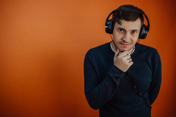 Een mooie jongeman in een koptelefoon met oren danst op een oranje achtergrond. Het concept van Internationale Muziekdag. — Stockfoto