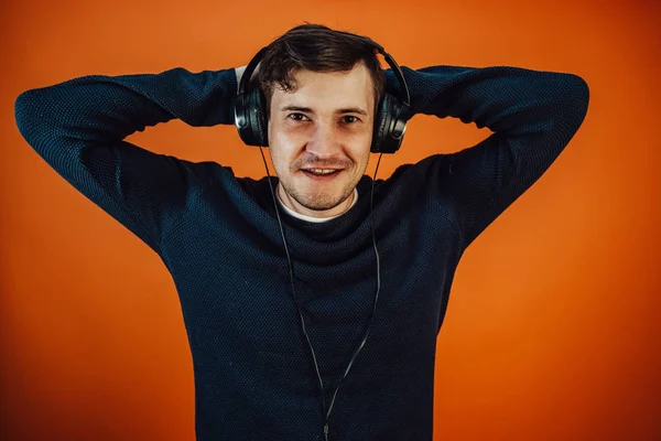 Ein schöner junger Mann mit Kopfhörern und Ohren tanzt auf orangefarbenem Hintergrund. Das Konzept des Internationalen Tages der Musik. — Stockfoto