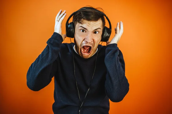 Ein schöner junger Mann mit Kopfhörern und Ohren tanzt auf orangefarbenem Hintergrund. Das Konzept des Internationalen Tages der Musik. — Stockfoto