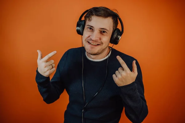 Een mooie jongeman in een koptelefoon met oren danst op een oranje achtergrond. Het concept van Internationale Muziekdag. — Stockfoto