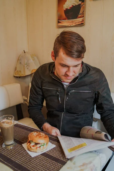 A man reading a newspaper sitting at the table. A male learns the latest news by reading the press. A man reading a newspaper in a cafe at Breakfast.