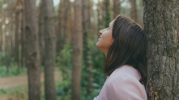 Serieuze vrouw kijkt uit van achter de boom. Mooie rustige vrouw aanraken boom en kijken naar camera in rustig bos — Stockfoto