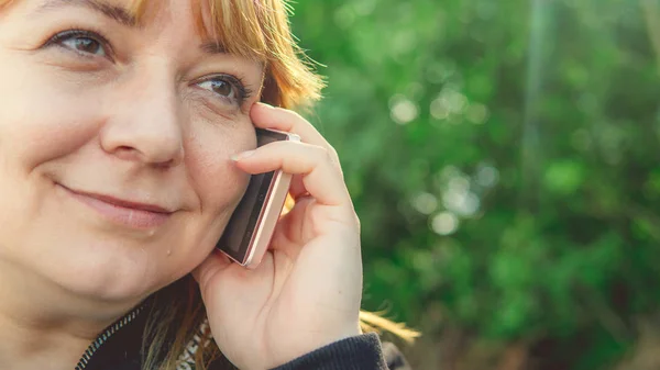 Uma mulher adulta falando em um smartphone, close-up. Feminino falando no telefone celular e olhando para longe. Mulher bonita falando no telefone enquanto caminhava — Fotografia de Stock