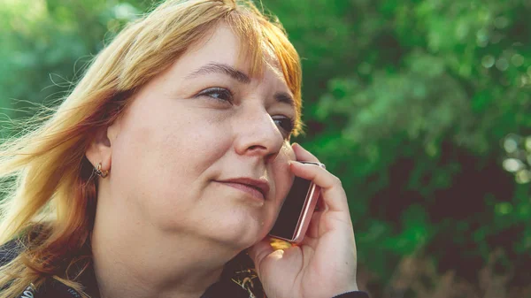 Uma mulher adulta falando em um smartphone, close-up. Feminino falando no telefone celular e olhando para longe. Mulher bonita falando no telefone enquanto caminhava — Fotografia de Stock