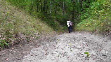 Parkta yürüyen isimsiz bir kadın. Süslü sırt çantalı genç bir bayanın arka görüntüsü. Sessiz sonbahar parkında yol boyunca yürüyor.
