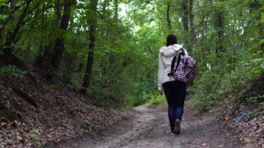 Parkta yürüyen isimsiz bir kadın. Süslü sırt çantalı genç bir bayanın arka görüntüsü. Sessiz sonbahar parkında yol boyunca yürüyor.