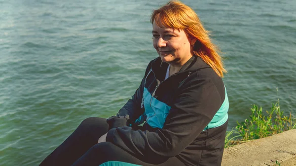 Una guapa joven vestida con ropa casual se encuentra sentada en la retaguardia cerca del agua.. — Foto de Stock