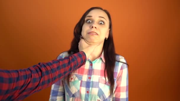 Een mannenhand in een shirt wurgt een bange jonge vrouw op een oranje achtergrond. Het concept van het stoppen van huiselijk geweld tegen vrouwen. — Stockvideo