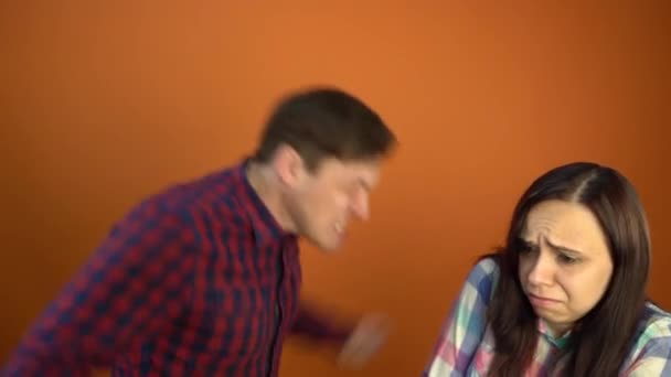Szalony i agresywny mężczyzna krzyczy na wystraszoną młodą kobietę na pomarańczowym tle. Koncepcja zaprzestania przemocy domowej wobec kobiet. — Wideo stockowe