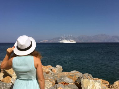 Güneşli bir günde, beyaz şapkalı ve elbiseli genç bir kadın denize bakıyor. Konsept: Turizm ve seyahat.