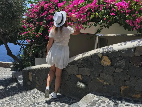 Mladá žena v bílých šatech a bílý klobouk má vůni květin za slunečného dne. — Stock fotografie