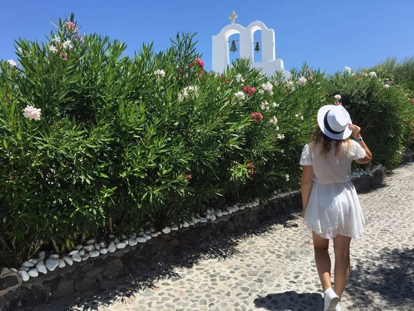 Una joven con un vestido blanco y un sombrero blanco en el fondo de la histórica iglesia ortodoxa griega en Santorini, Grecia . — Foto de Stock