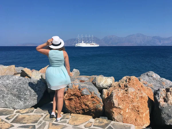 Una joven vestida y un sombrero blanco miran al mar en un día soleado. Concepto: turismo y viajes. — Foto de Stock