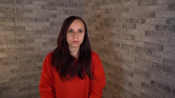 Kırmızı kapüşonlu genç bir kadın tuğla bir arka planda kamerada konuşuyor. Bir kadın blogcu vlog 'unu yönetiyor. — Stok video