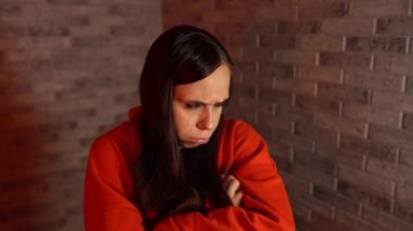 Kırmızı kapüşonlu güzel bir kadın kötü bir ruh hali içinde. Genç bir kadın, tuğladan bir arka planda üzüntü gösterir..