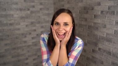 Ekose gömlekli güzel duygusal bir kadın, elleri tuğla bir arka planda yanaklarında gezerken hoş bir şekilde şaşırır..