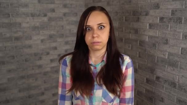 Uma jovem mulher em uma camisa xadrez ressentimentos e expressa suas emoções negativas em um fundo de tijolo. — Vídeo de Stock